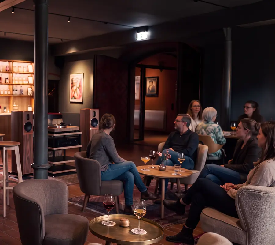 Mehrere Personen sitzen in Sesseln und hören einer HIFI-Anlage von in-akustik in einem stilvollen Raum mit beleuchtetem Regal zu.