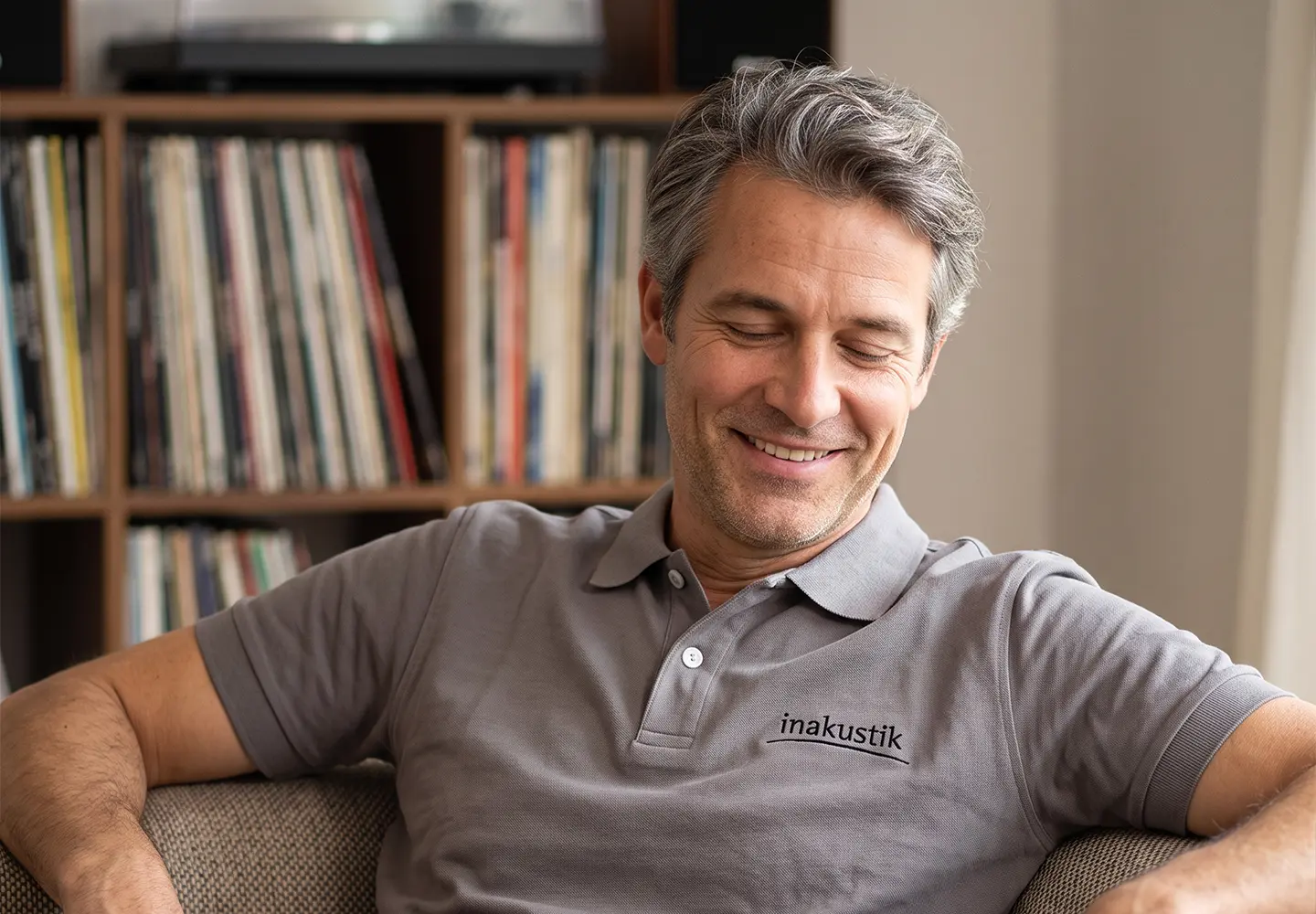 Mann trägt das in-akustik Polo-Shirt, sitzt auf einem Sofa und hört Musik.